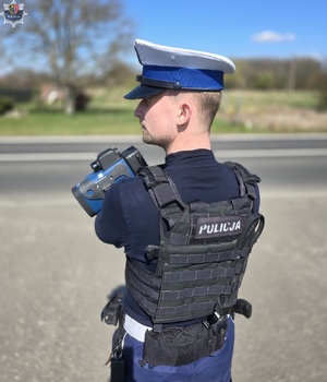 Policjant stojący tyłem, trzyma w ręku ręczny pomiar prędkości