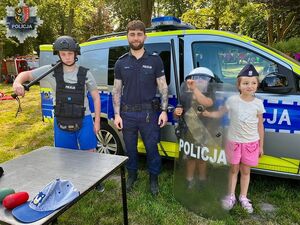 Policjant stoi obok dzieci na tle radiowozu