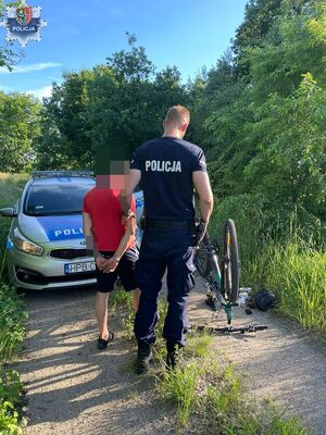 policjant z mężczyzną w kajdankach na tle radiowozu