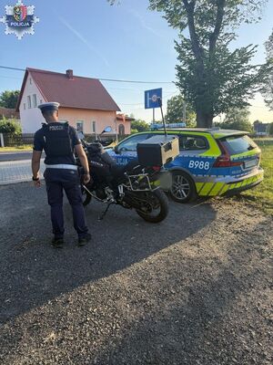 policjant stoi obok radiowozu oraz motocyklu